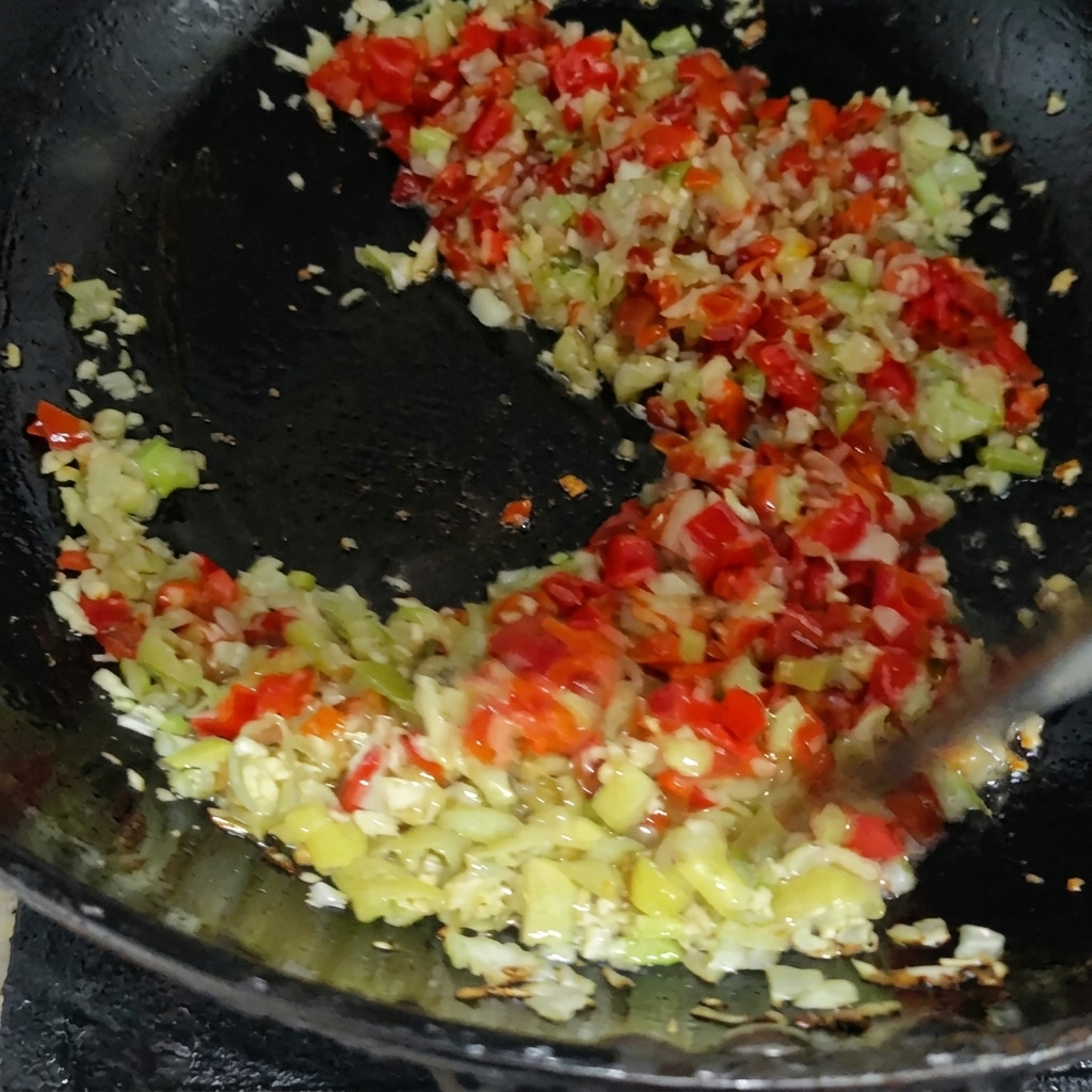 A colorful mixture of minced red and green chilis being sautéed with other aromatics in a hot pan.
