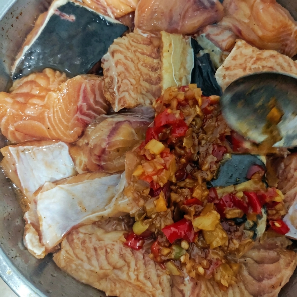A metal plate filled with raw fish pieces being topped with a thick, chunky red chili and garlic sauce using a spoon.
