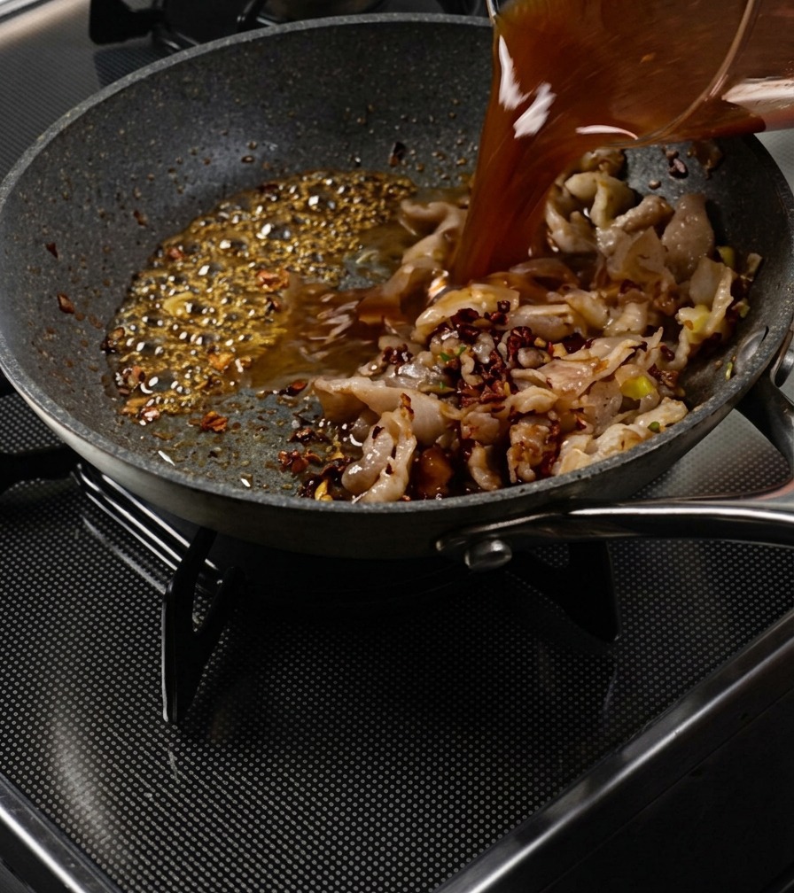 Savory brown sauce being poured from a measuring cup into a pan containing sautéed pork and bubbling caramel.