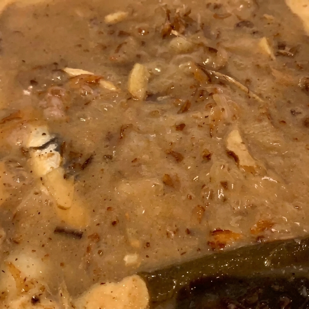 A tight close-up of brown dried fish flakes and small fish bubbling inside a thick, tan-colored simmering liquid.