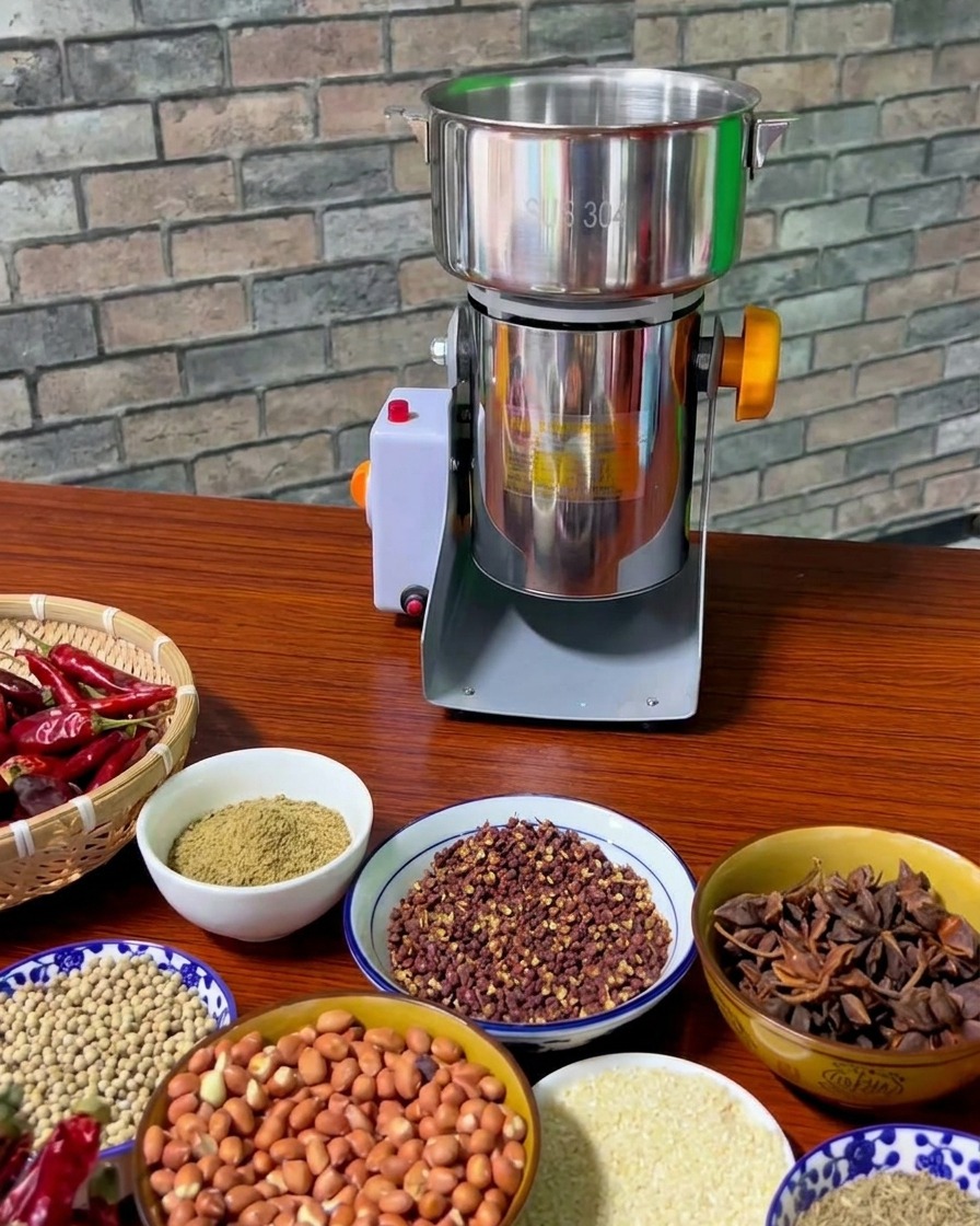 An assortment of bowls containing toasted Sichuan peppercorns, peanuts, star anise, and fennel seeds arranged on a wooden table next to a stainless steel electric spice grinder.