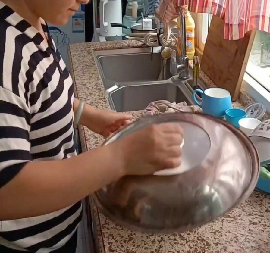 A person placing a large metal lid over a bowl containing dough to let it rest.