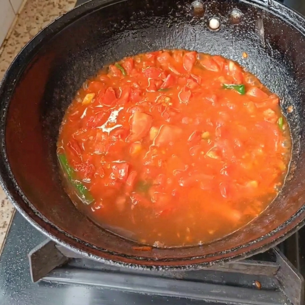 Diced tomatoes and green onions simmering in water inside a black wok on a gas stove.