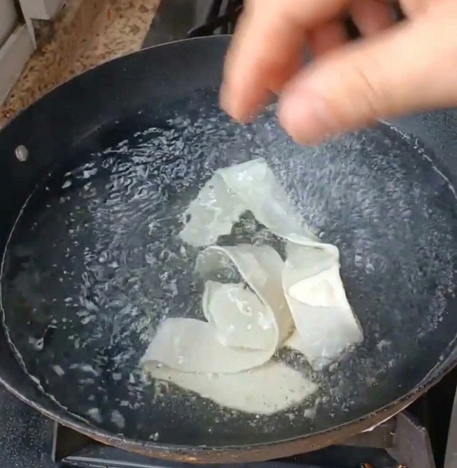 Wide noodle ribbons and green leafy vegetables being submerged into a pan of bubbling, boiling water.
