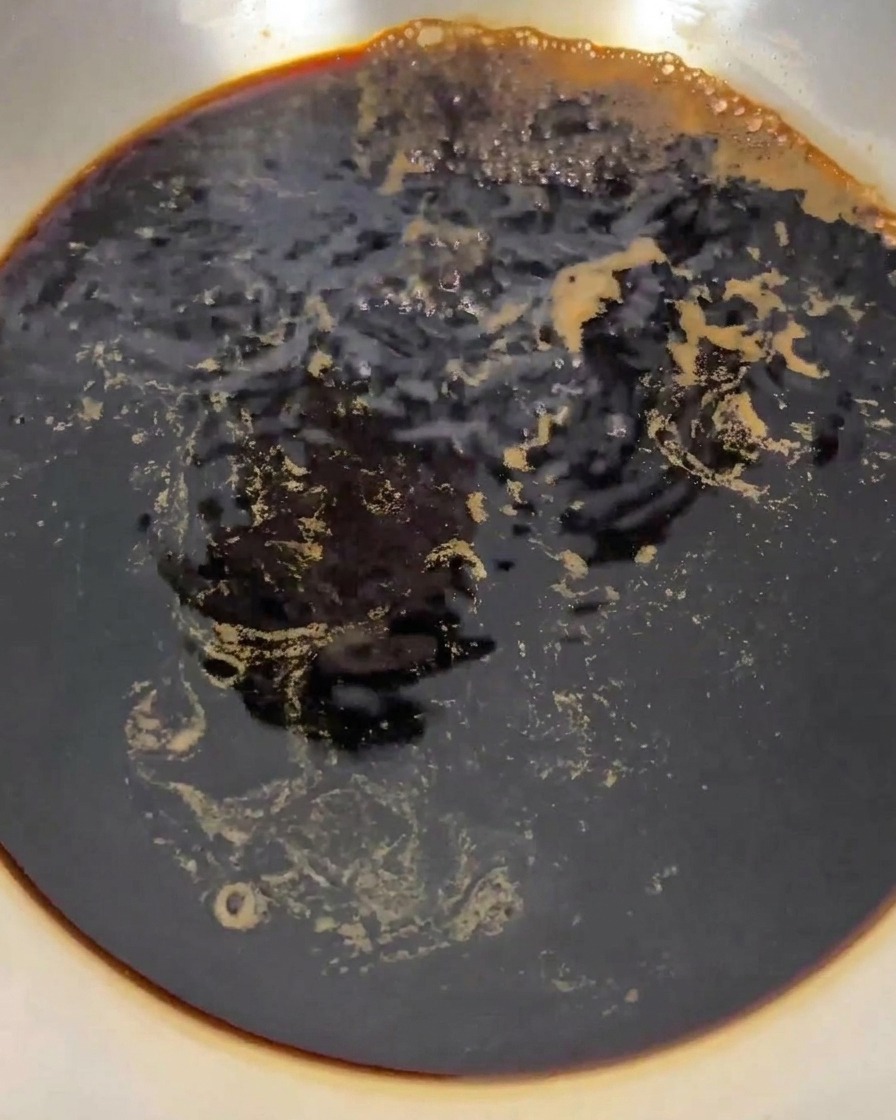 The dark liquid mixture bubbling and boiling vigorously in a stainless steel pan on the stove.