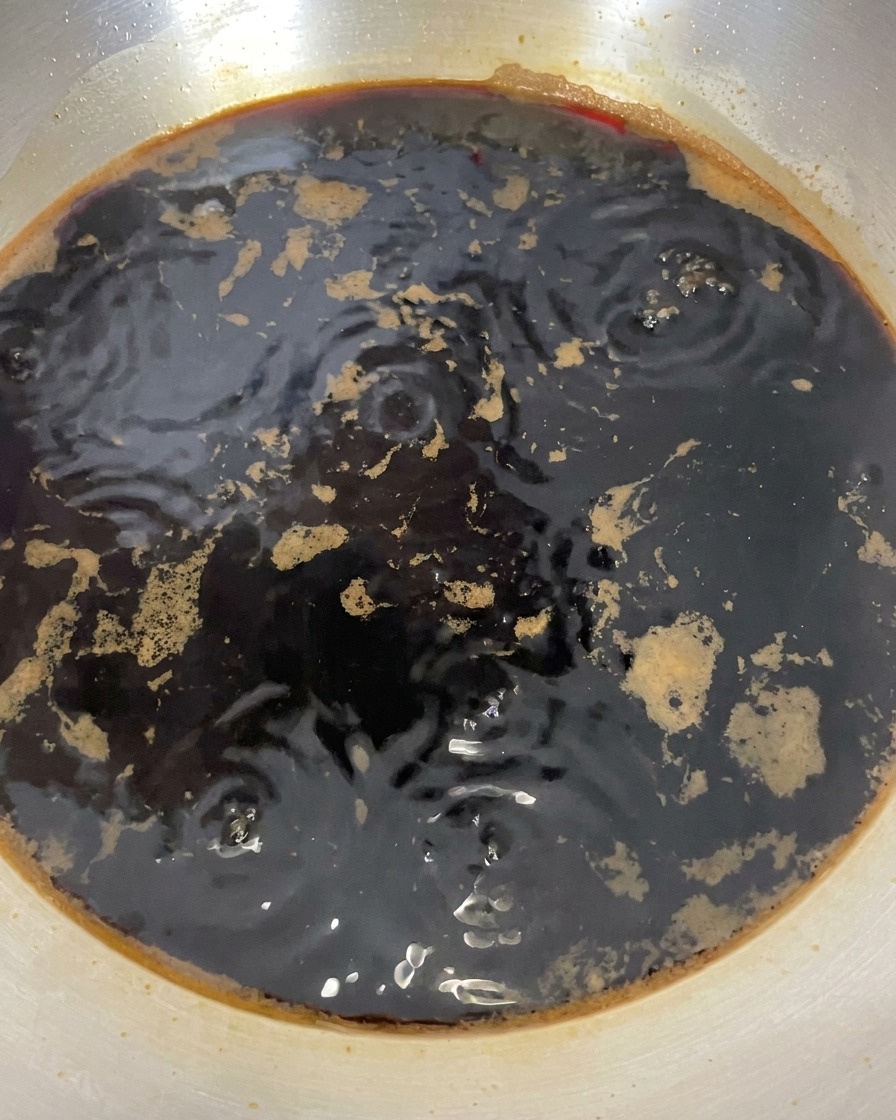 The dark soy sauce mixture in a pan showing small bubbles after the heat has been turned off.