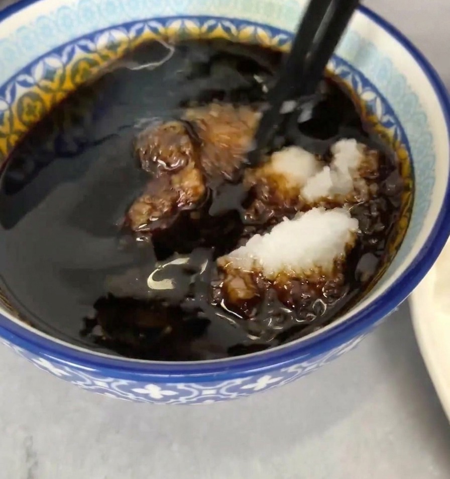 A blue and white patterned bowl filled with dark soy-based dipping sauce, with a portion of white grated radish being stirred in using black chopsticks.