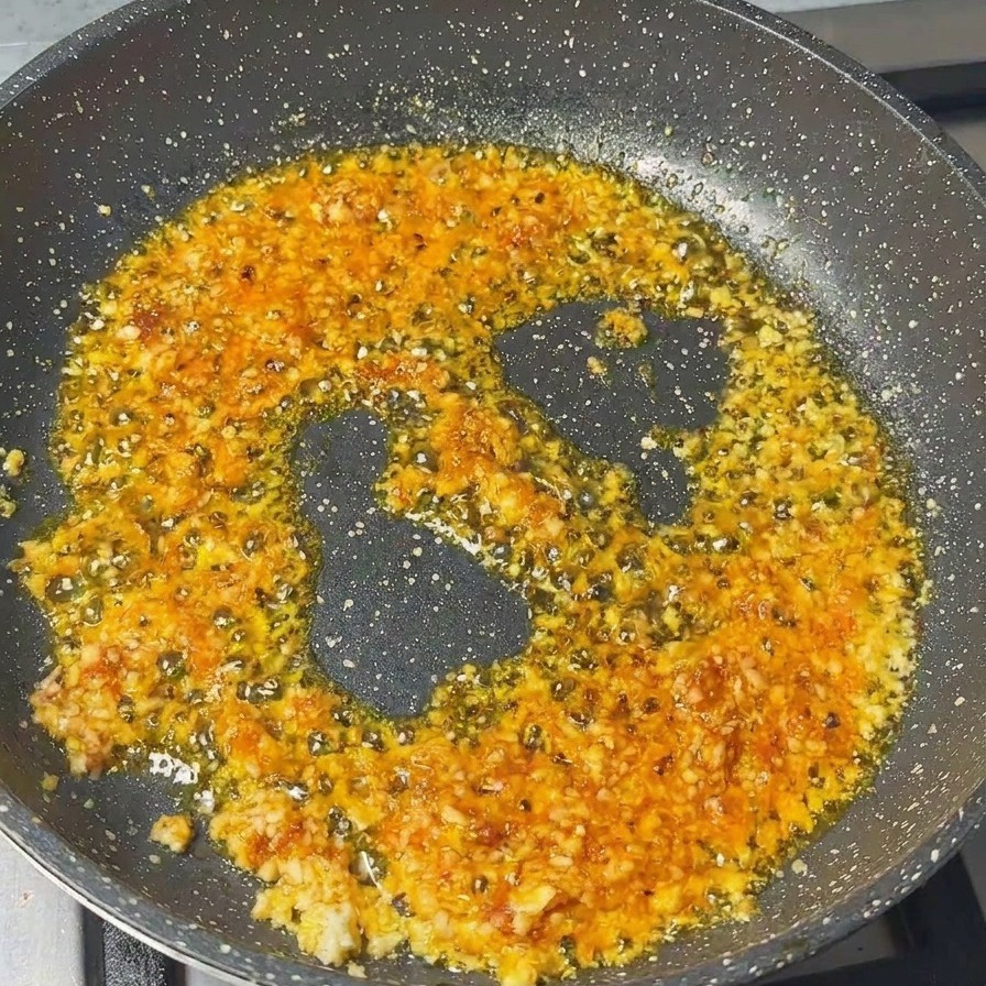 Ground pork being stirred into a pan with a base of minced garlic and shrimp paste.
