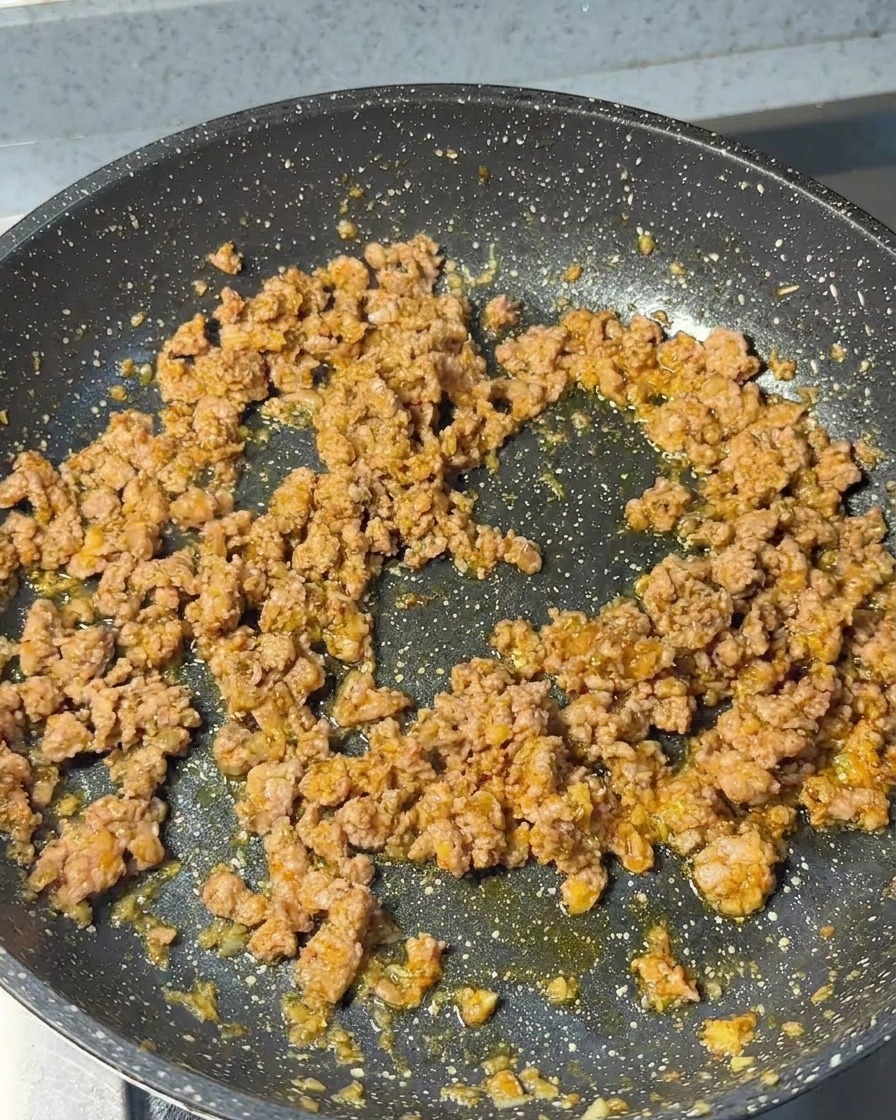 Ground pork being stir-fried in a pan with aromatics, showing a browned and crumbly texture.