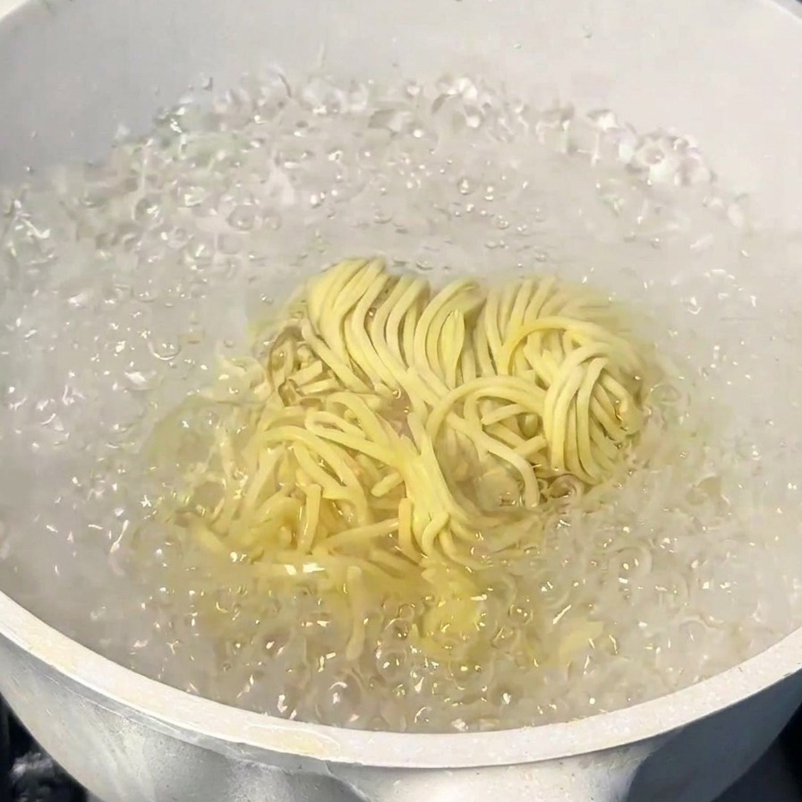 A bundle of yellow Japanese ramen noodles being cooked in a pot of vigorously boiling water.