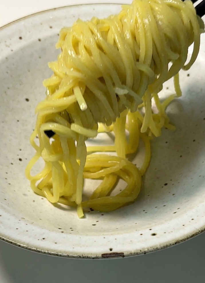 Cooked yellow noodles being lifted with chopsticks and placed into a light-colored ceramic serving bowl.