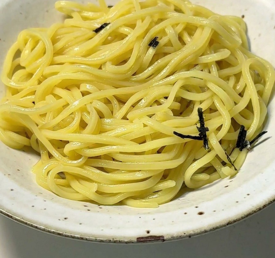 A white ceramic bowl filled with yellow ramen noodles topped with strips of shredded black seaweed.