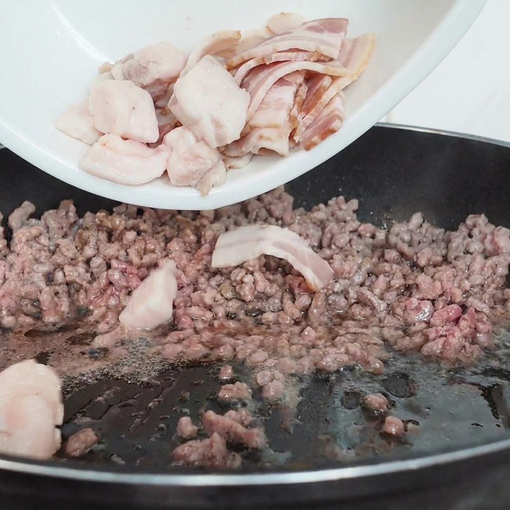Sliced white mushrooms being poured from a white plate into a black frying pan containing partially cooked ground beef.