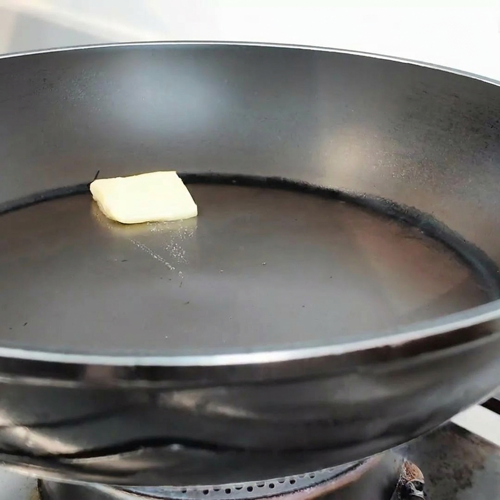 A small pat of yellow butter melting in the center of a clean black frying pan.
