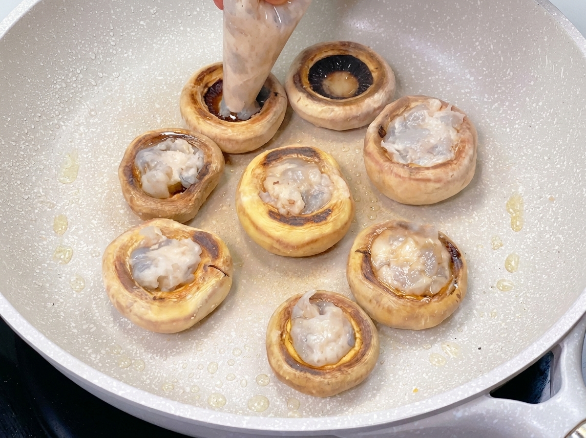 A plastic piping bag filling the hollow center of a seared mushroom cap with a smooth, translucent shrimp paste.