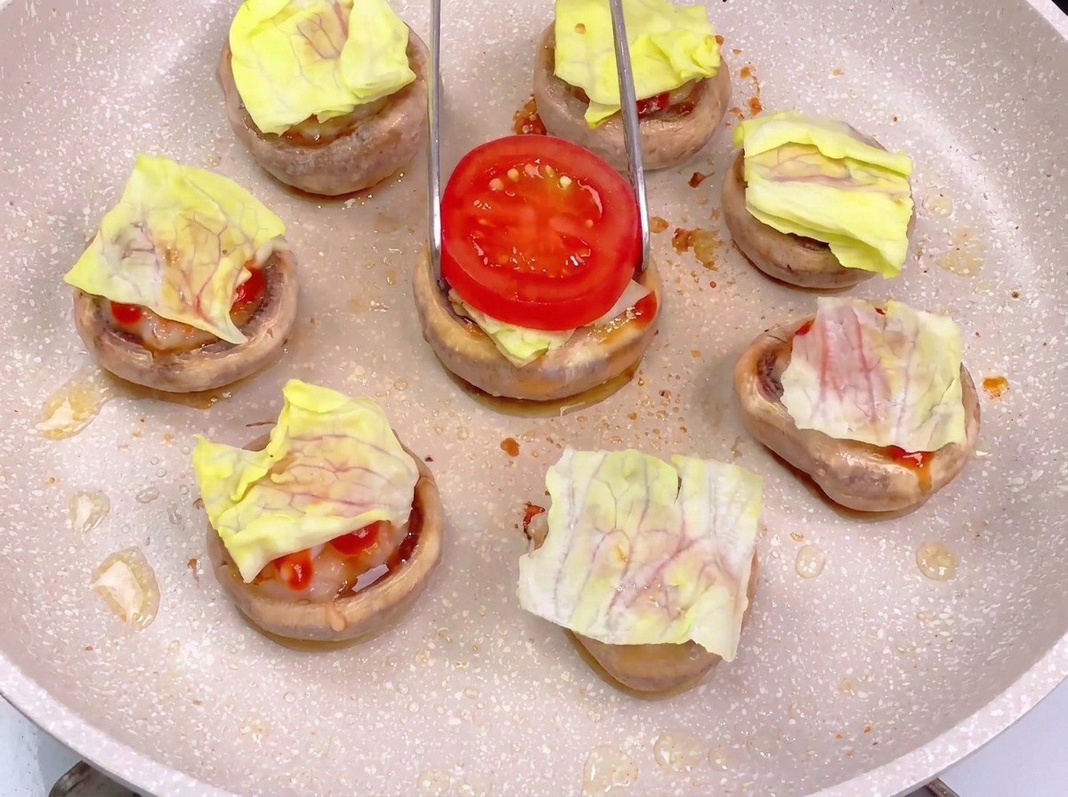 Using tongs to place a bright red tomato slice onto a mushroom burger base already layered with lettuce and sauces.