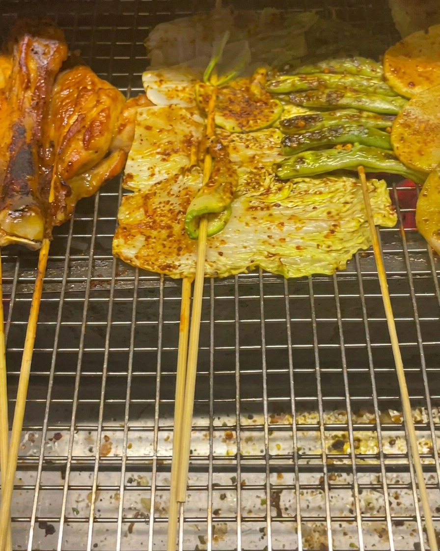 Chicken thighs, baby cabbage, zucchini, green beans, and potato slices grilling on a wire rack.