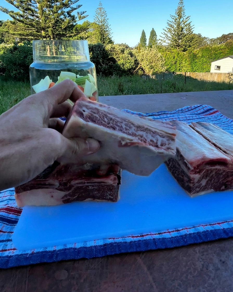 A hand holding a thick raw beef short rib over a glass jar filled with chopped vegetables.