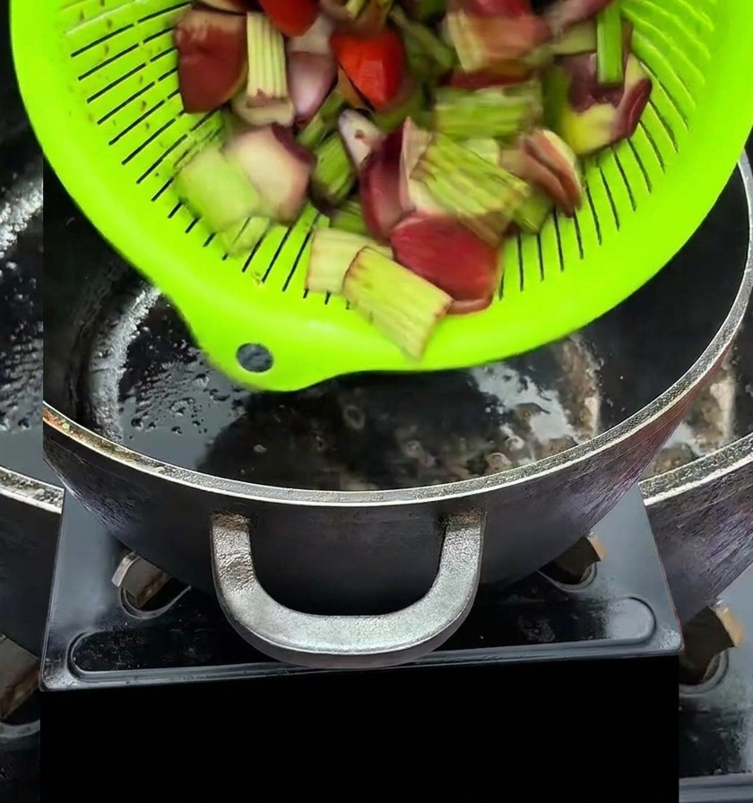 Chopped vegetables being poured from a bright green colander into a hot black pot.