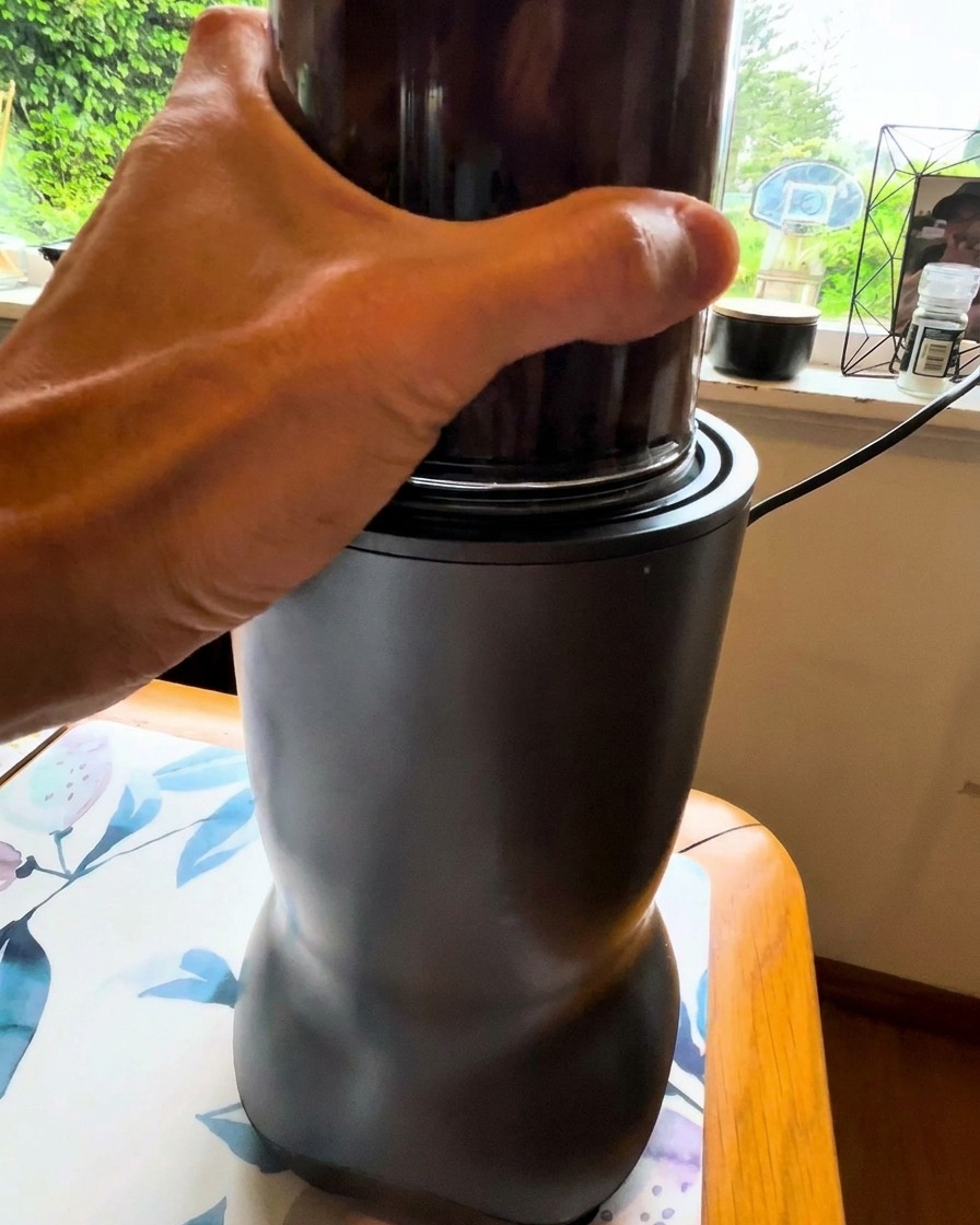 A hand holding a small blender cup as it blends a dark vegetable mixture.
