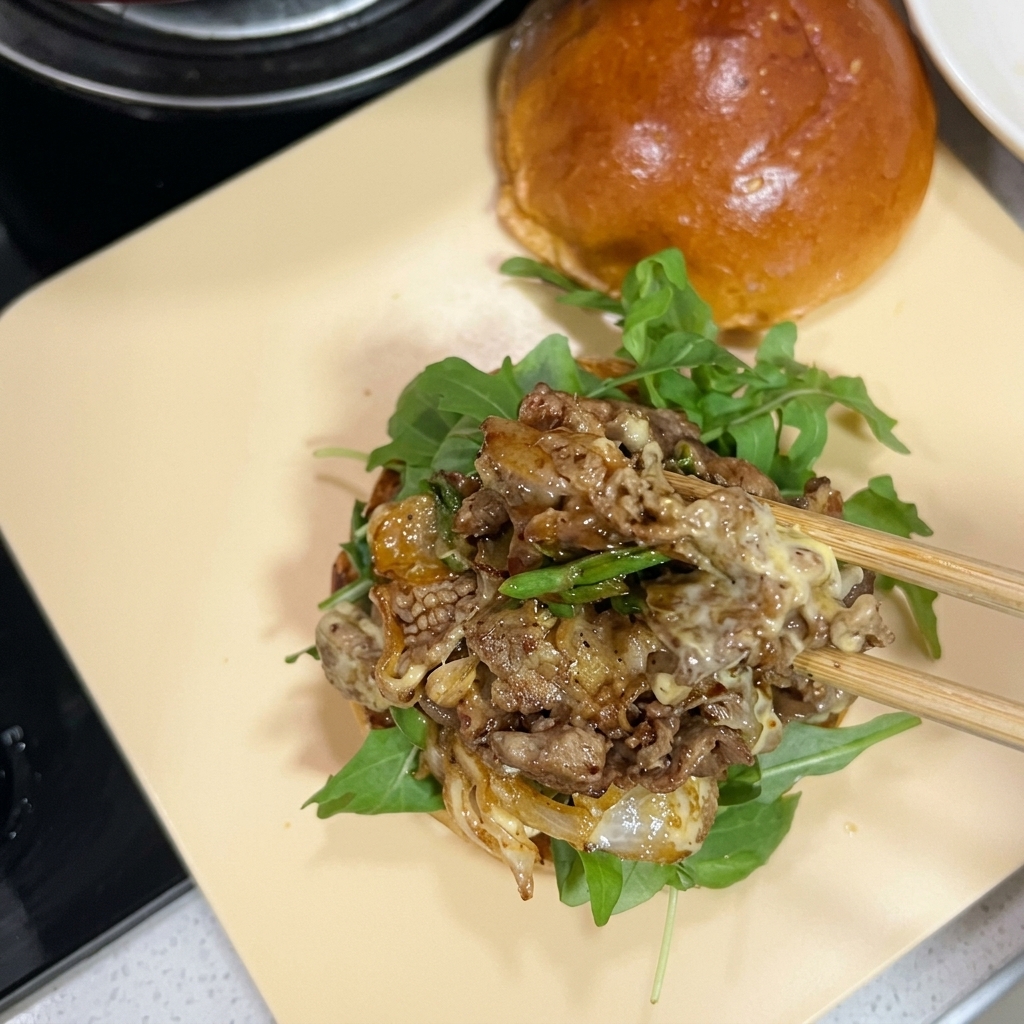 Chopsticks transferring a savory mound of stir-fried beef with melted cheese onto a burger bun layered with arugula.