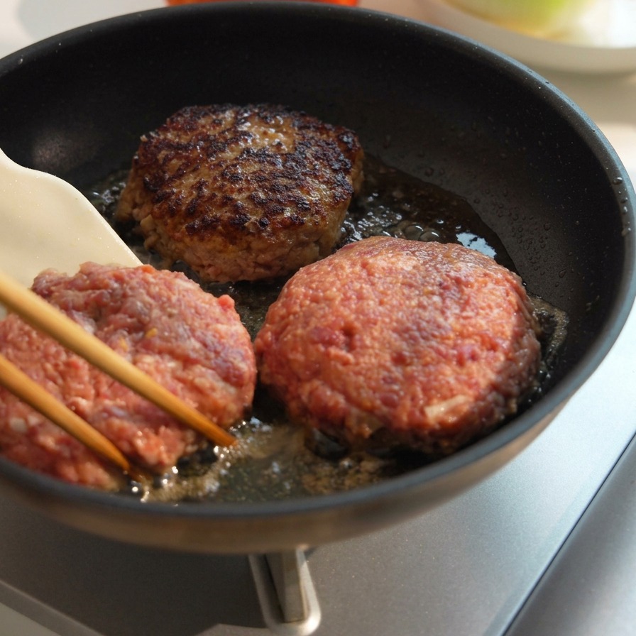 Three thick beef patties cooking in a pan, with one flipped over to show a deeply browned and caramelized crust.