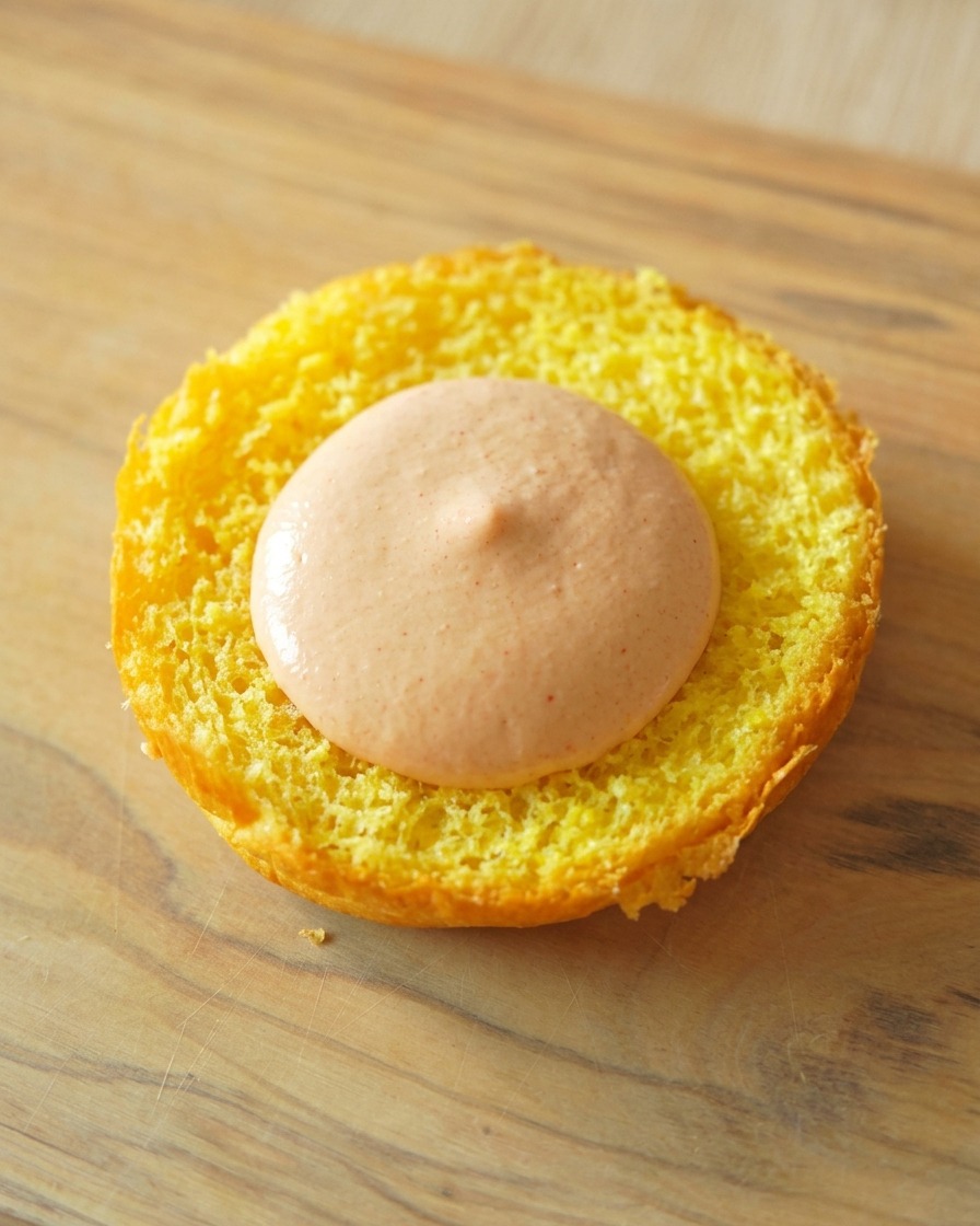 The toasted bottom of a yellow brioche bun with a smooth dollop of orange burger sauce spread in the center.