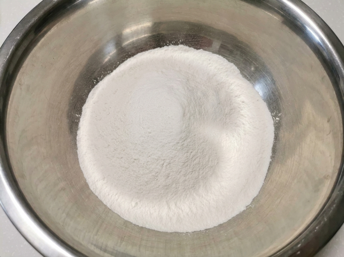 A pristine white mound of mixed rice flour and all-purpose flour sitting inside a large, clean stainless steel mixing bowl.