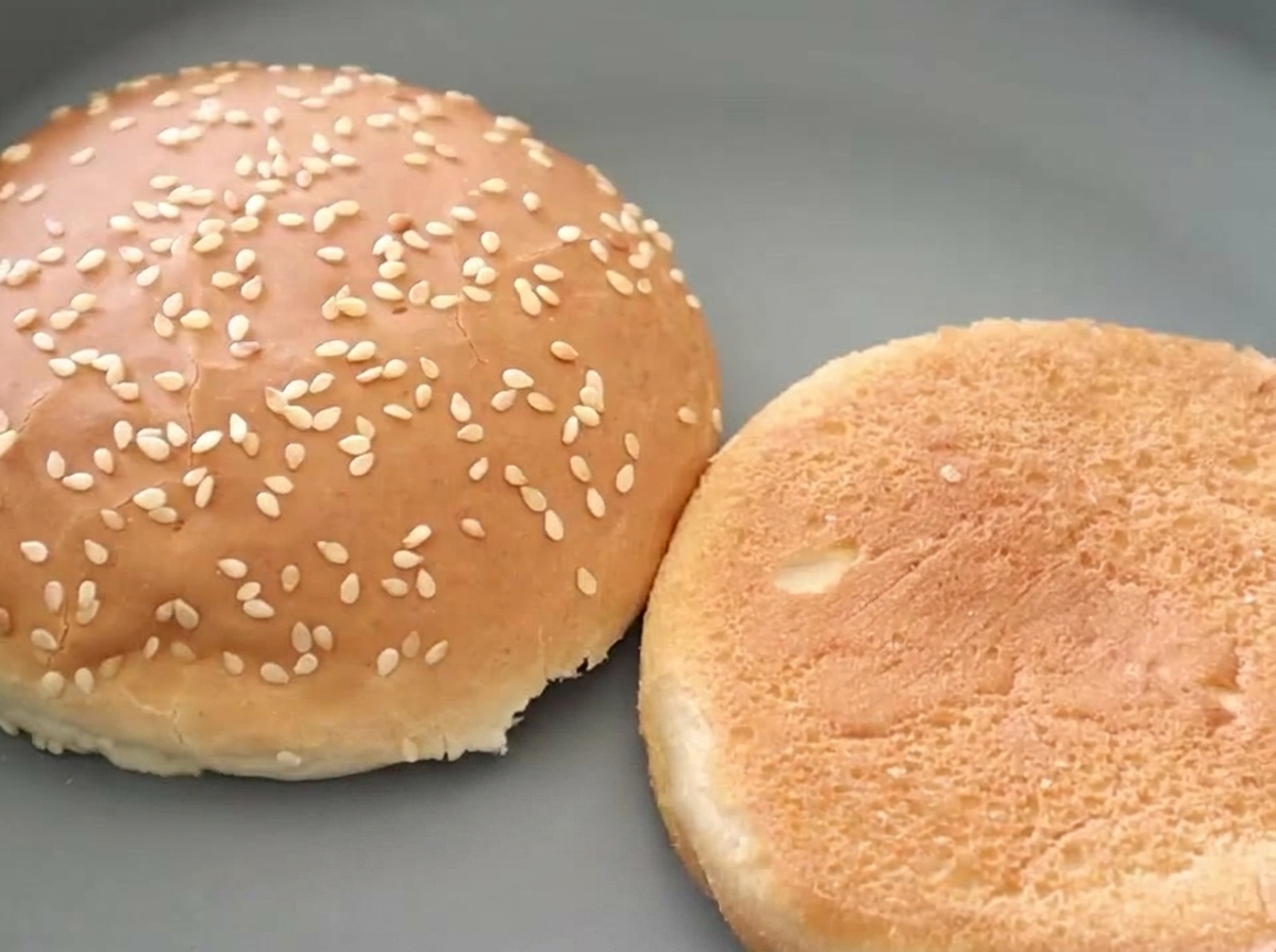 Two halves of a sesame seed burger bun shown side-by-side, with one revealing a beautifully toasted, golden-brown interior.
