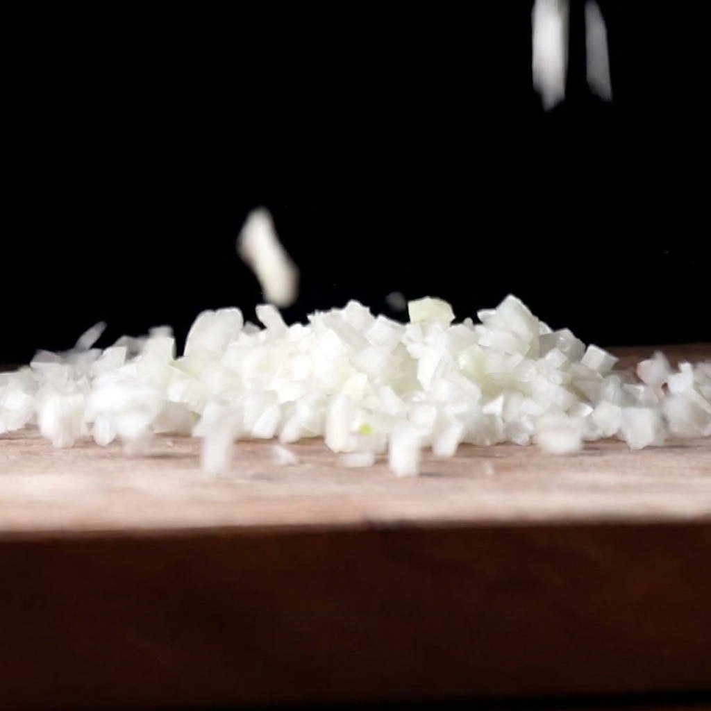 Finely diced white onion pieces falling onto a wooden cutting board against a dark background.
