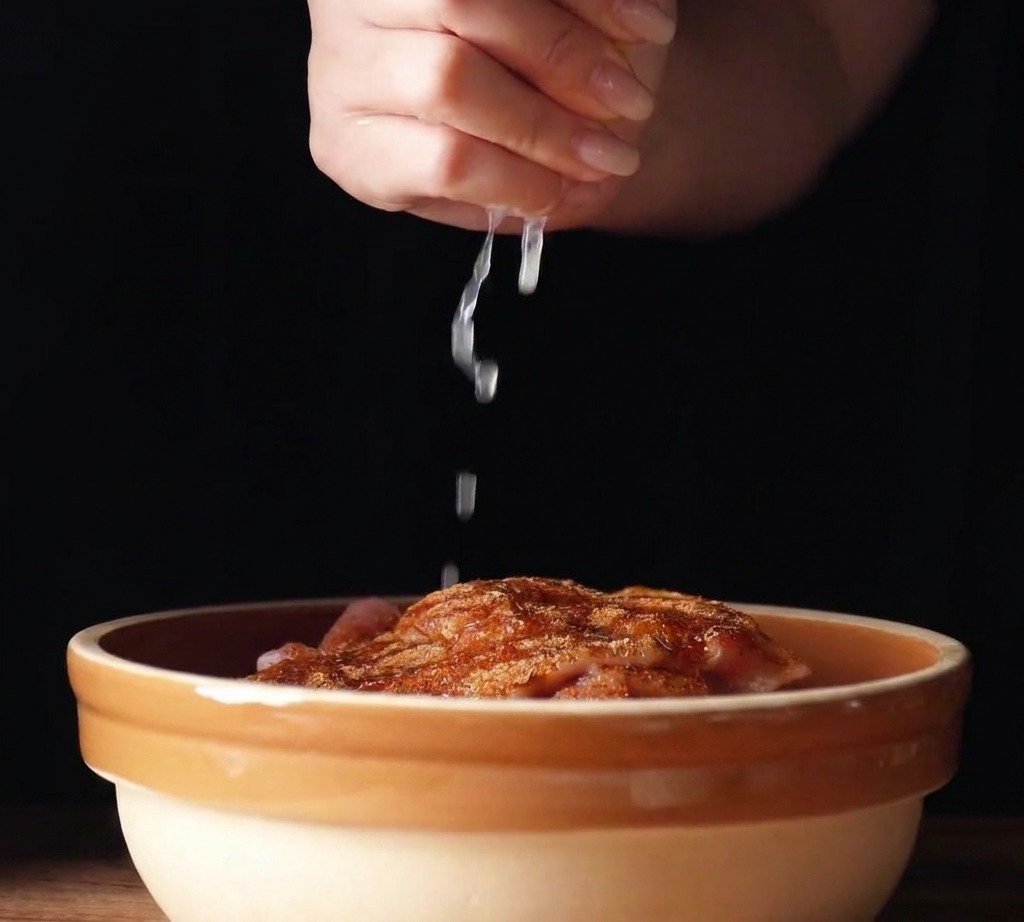 Fresh lemon juice being squeezed from a lemon wedge over seasoned chicken thighs in a ceramic bowl.