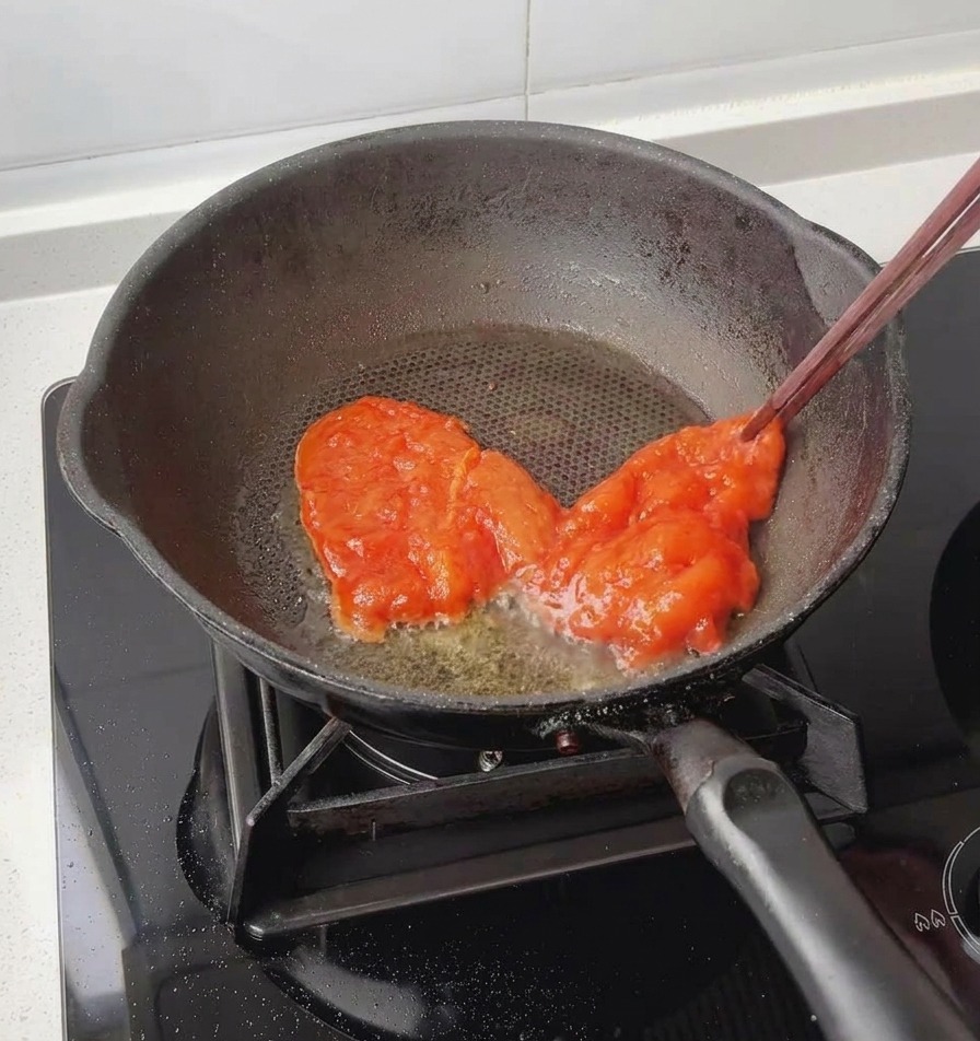 Using chopsticks to lower a red, fully marinated chicken breast into a lightly greased black frying pan.