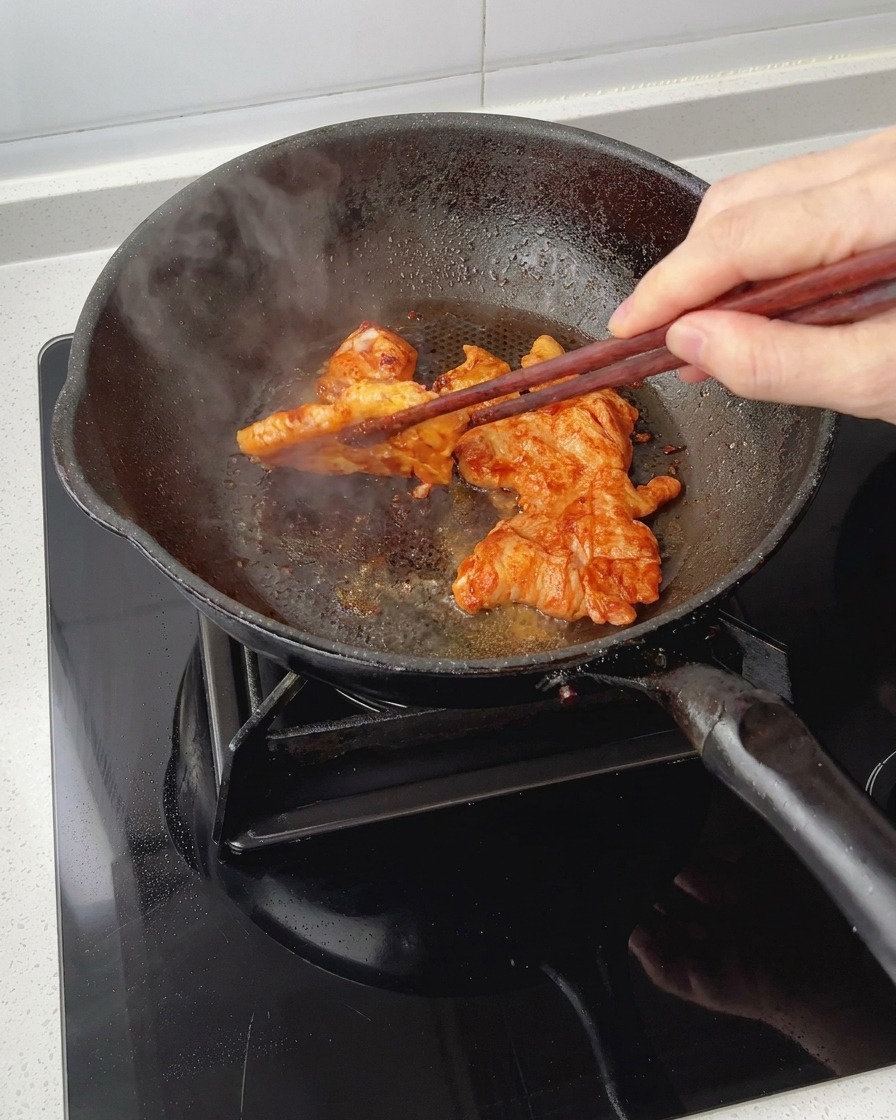 Searing marinated chicken breast pieces in a pan while flipping them over with chopsticks, showing a glossy, caramelized coating.