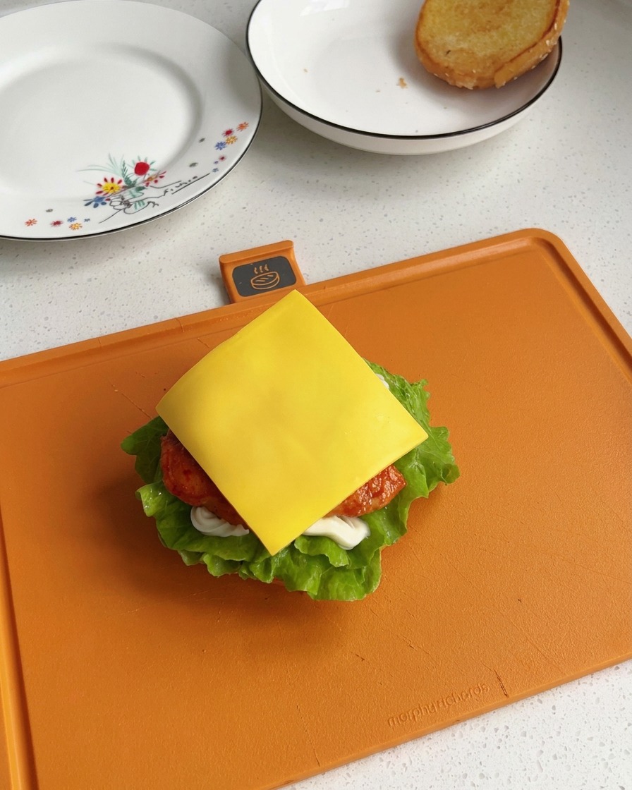A square slice of bright yellow processed cheese resting squarely on a freshly cooked chicken piece inside a partially assembled burger.
