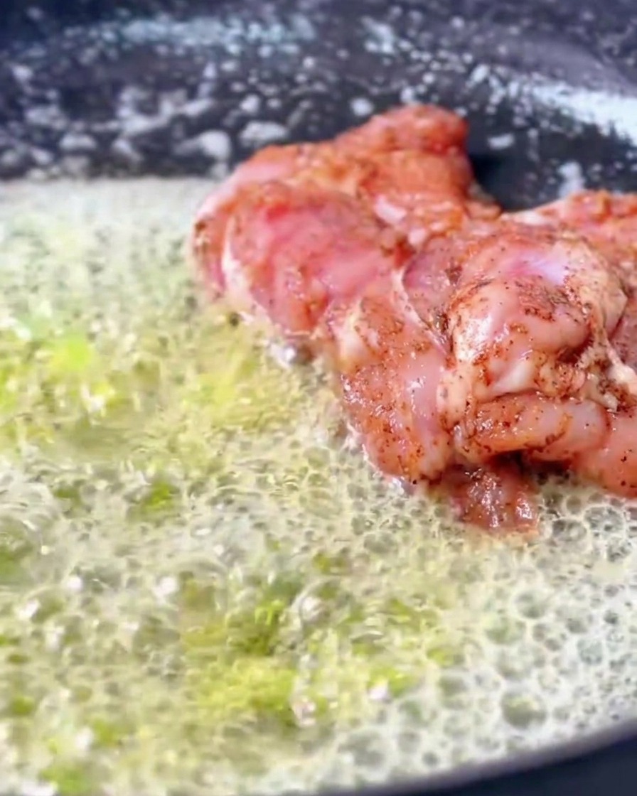 Marinated Cajun chicken thighs searing in a pan filled with a generous amount of bubbling, foaming melted butter.