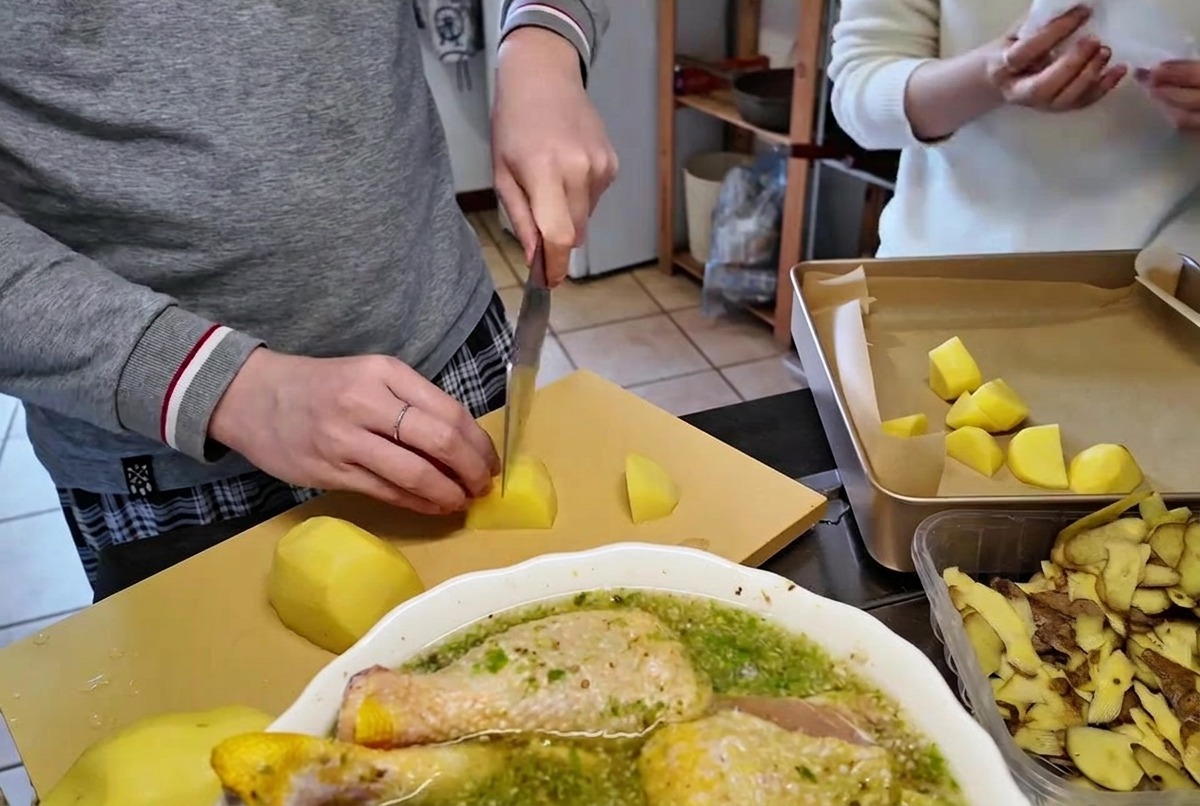 Slicing peeled raw potatoes into bite-sized pieces on a cutting board using a sharp kitchen knife.