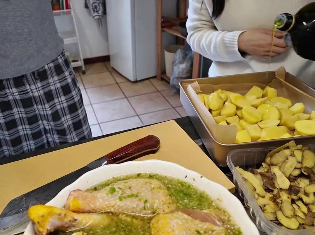 Pouring olive oil from a glass bottle onto a baking sheet filled with cut potato chunks.