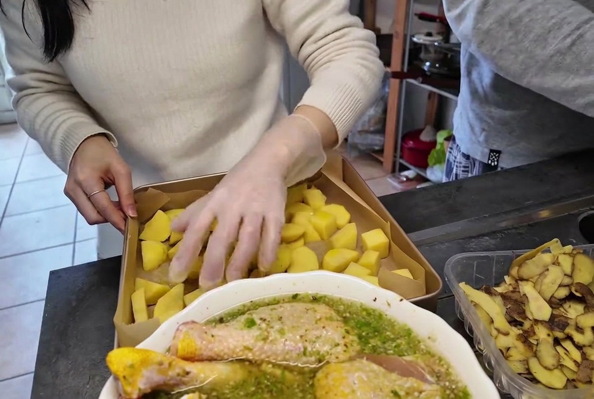 A hand in a clear plastic glove tossing and mixing potato pieces in a metal baking pan.