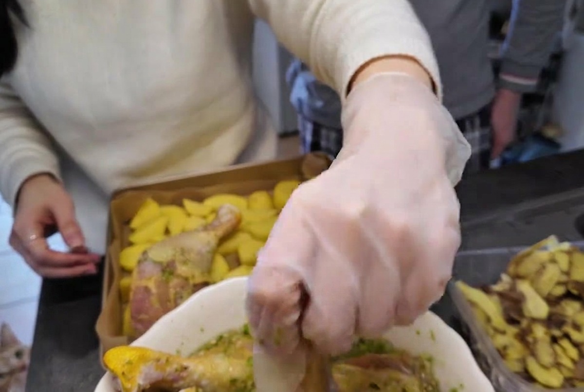 A gloved hand lifting a raw chicken drumstick coated in green herb marinade from a white bowl.