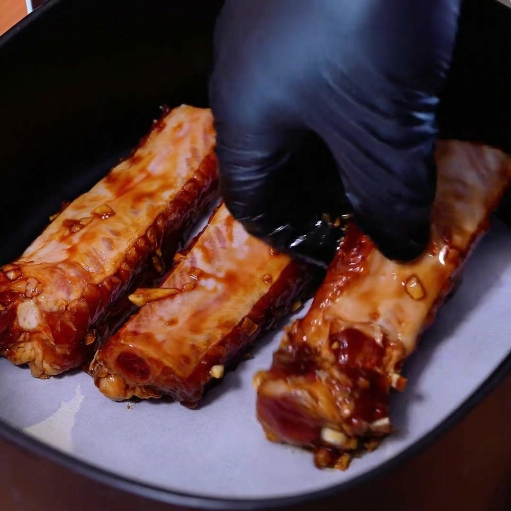 Marinated pork ribs neatly arranged side by side on parchment paper inside an air fryer basket.