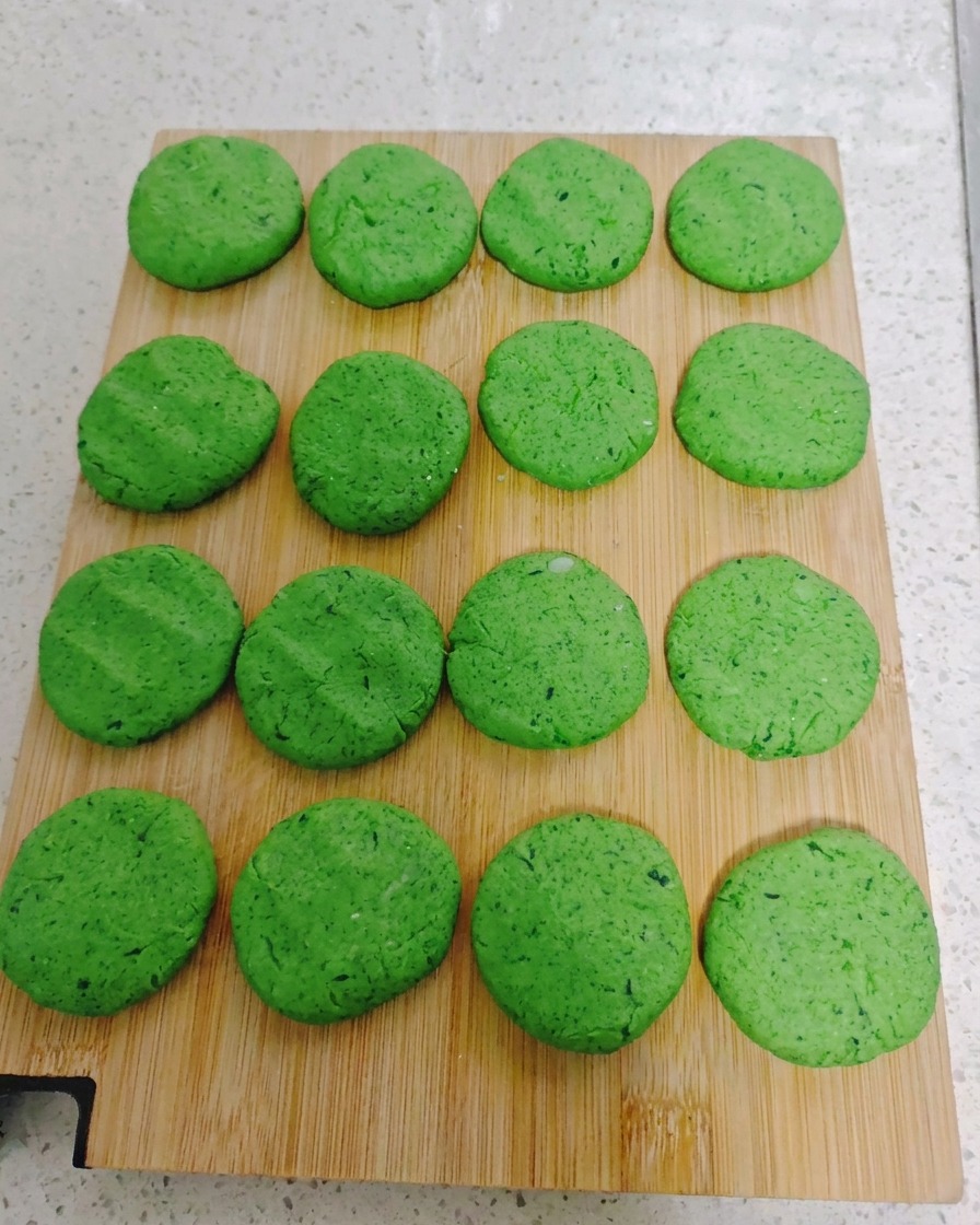 Sixteen round green vegetable pancake discs arranged in a neat grid pattern on a wooden cutting board.