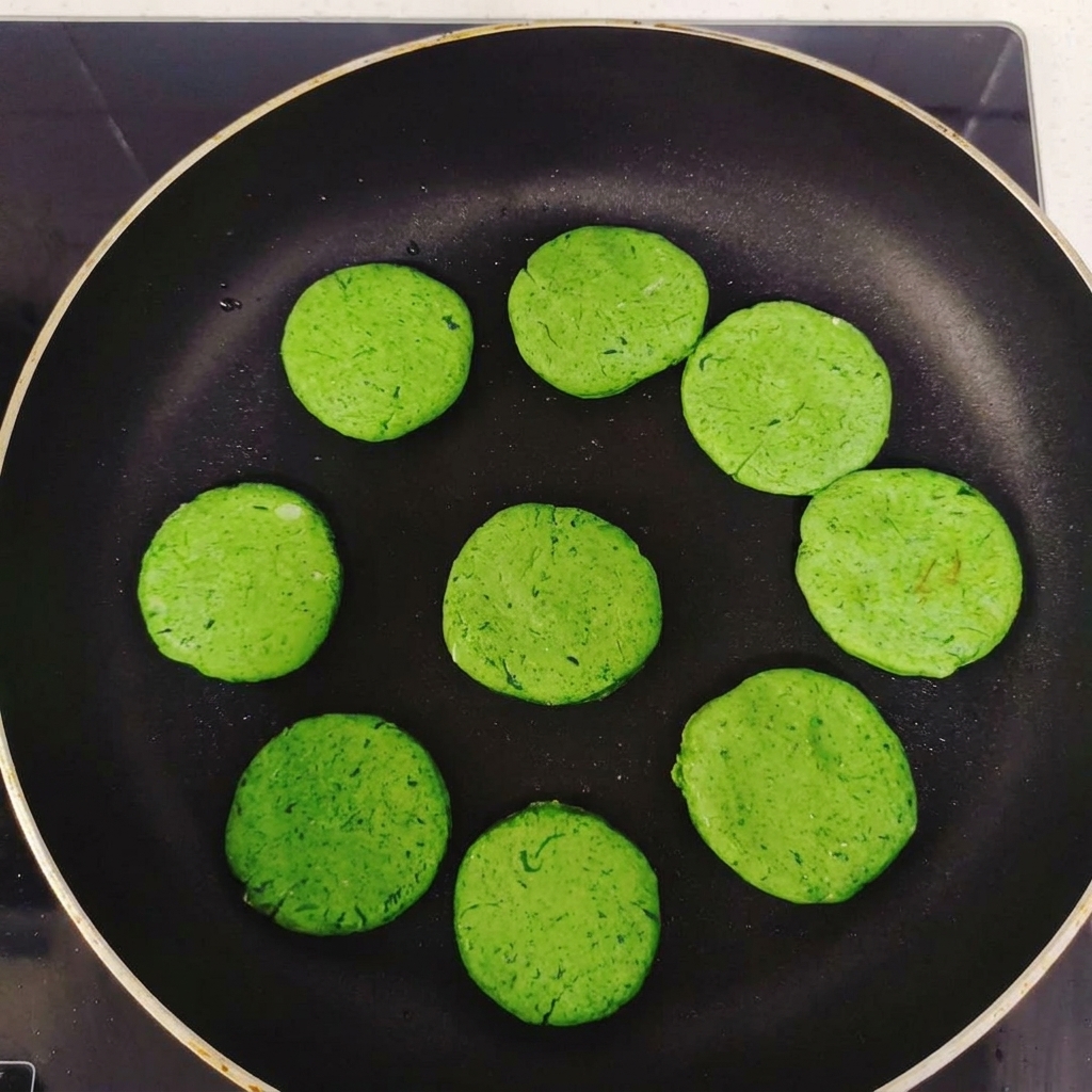 Multiple round green pancake discs arranged in a circle inside a black non-stick frying pan before cooking.