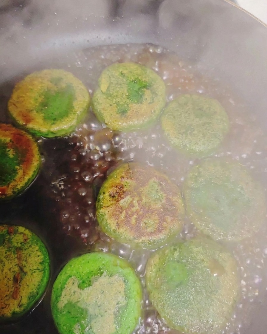 Water bubbling and creating steam around pan-seared green vegetable pancakes inside a hot pan.