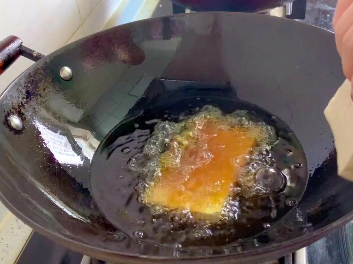 Slabs of old tofu being deep-fried in a wok of bubbling hot oil.