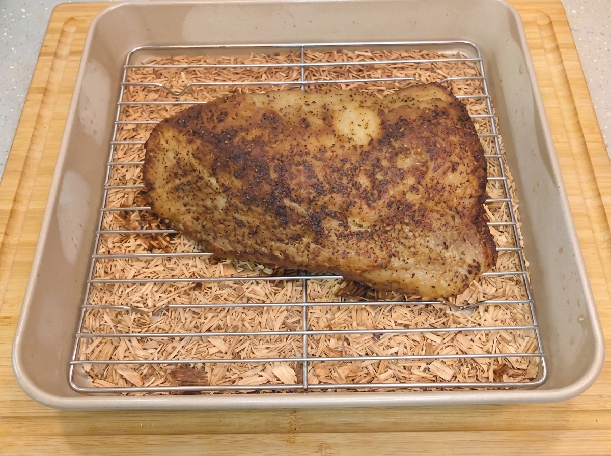 A hot, seasoned beef brisket resting on a metal wire rack inside a baking pan after the aluminum foil has been removed.
