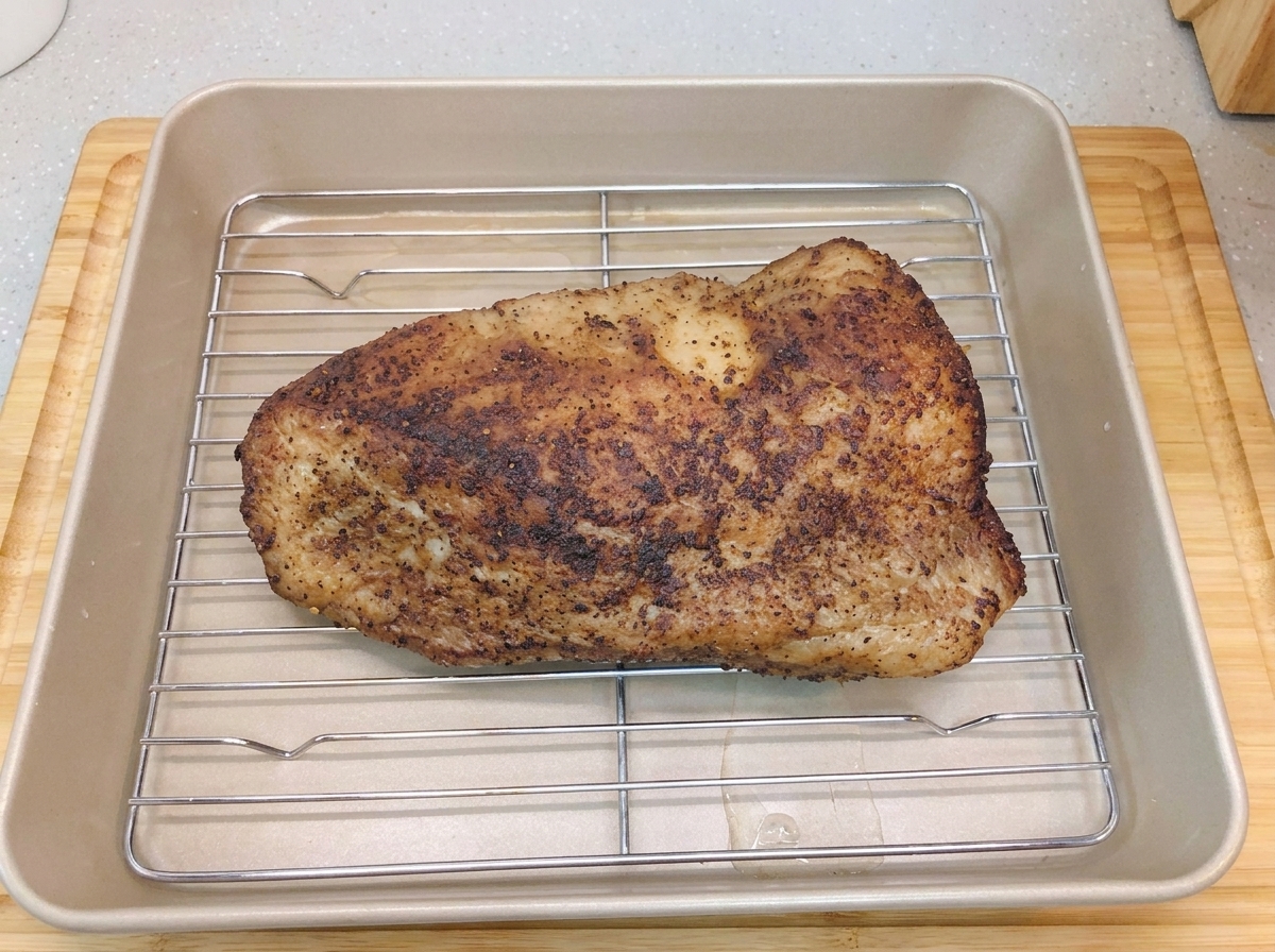 A seared beef brisket resting on a wire rack inside a golden baking pan with a layer of water at the bottom.