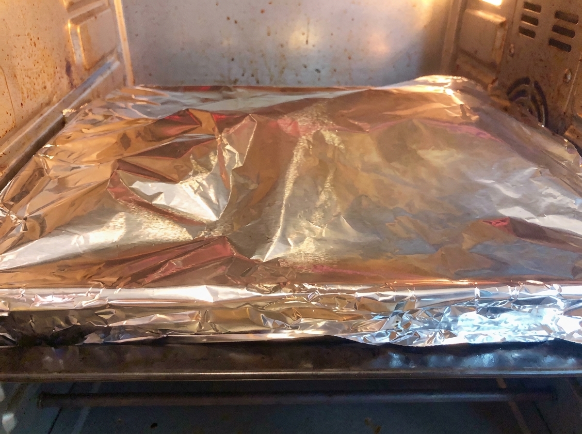 An aluminum foil-covered baking pan sitting inside a heated home oven for baking.