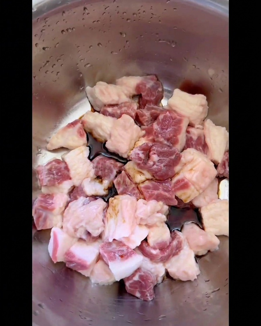 Dark soy sauce and liquid seasonings pooling around raw cubed beef brisket fat in a stainless steel bowl.