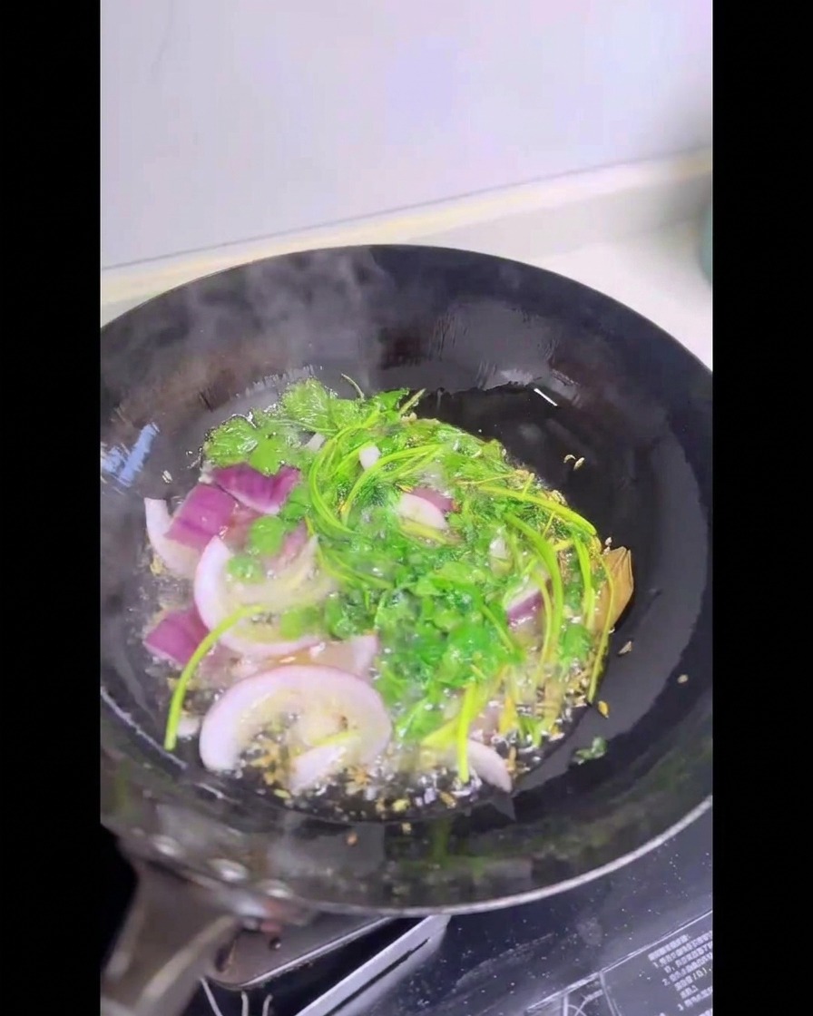 Fresh green cilantro stalks and sliced red onions sizzling inside a wok filled with hot shimmering oil.