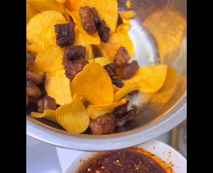 Crispy chunks of air-fried beef brisket fat tossed together with bright yellow ridged potato chips inside a stainless steel mixing bowl.